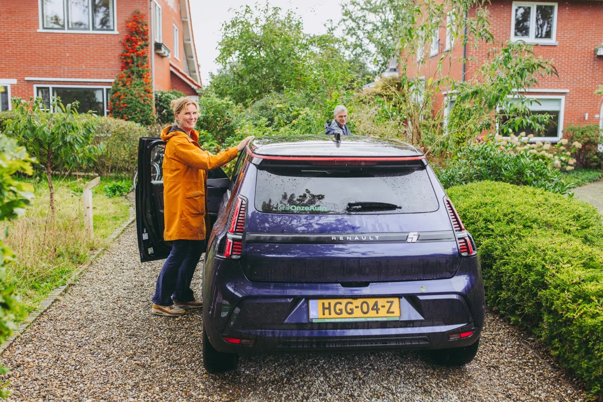 Persoon naast een deelauto op een oprit voor een huis.